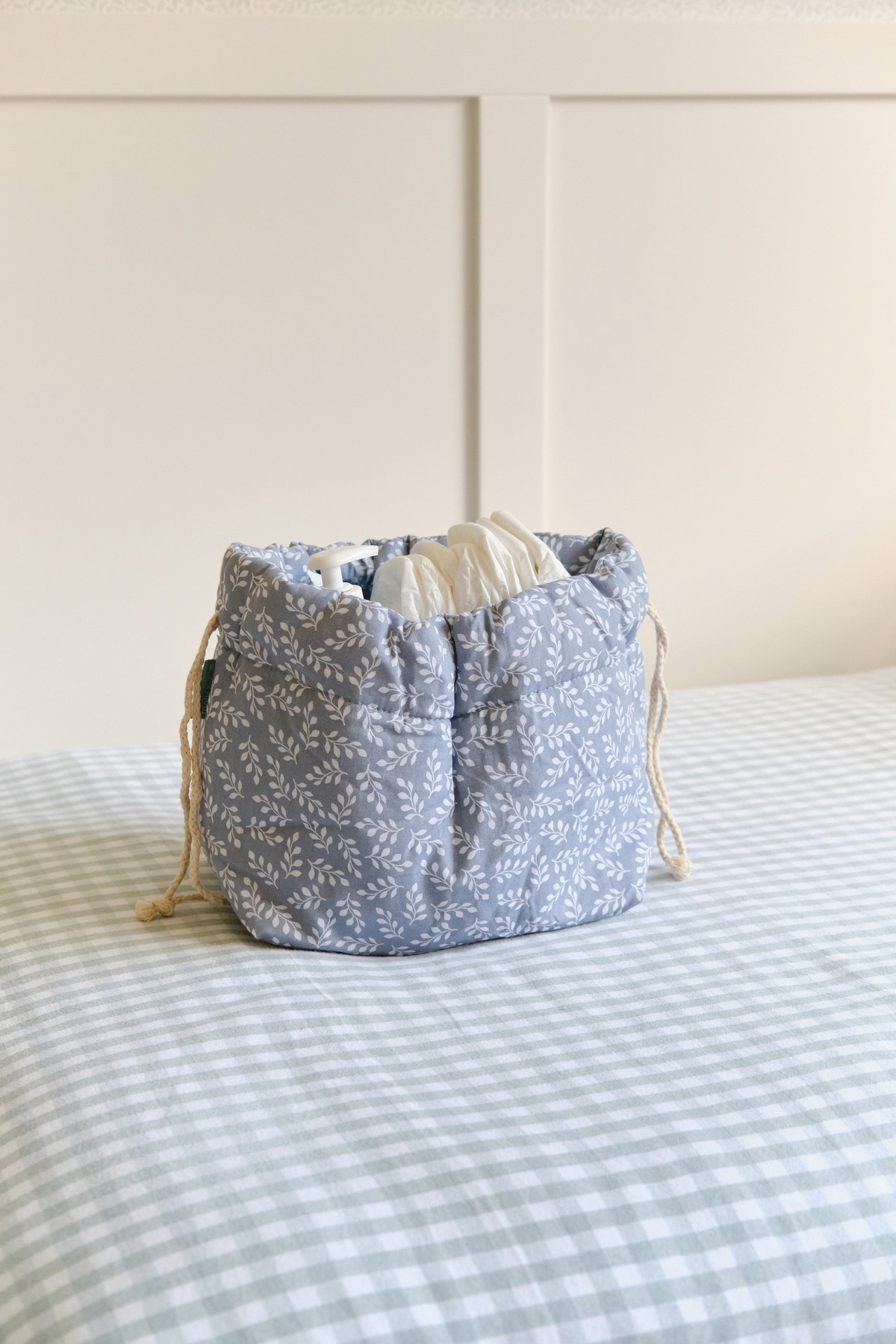 Cesto de tecido azul com padrão de folhas brancas contendo luvas e dispensador branco numa cama