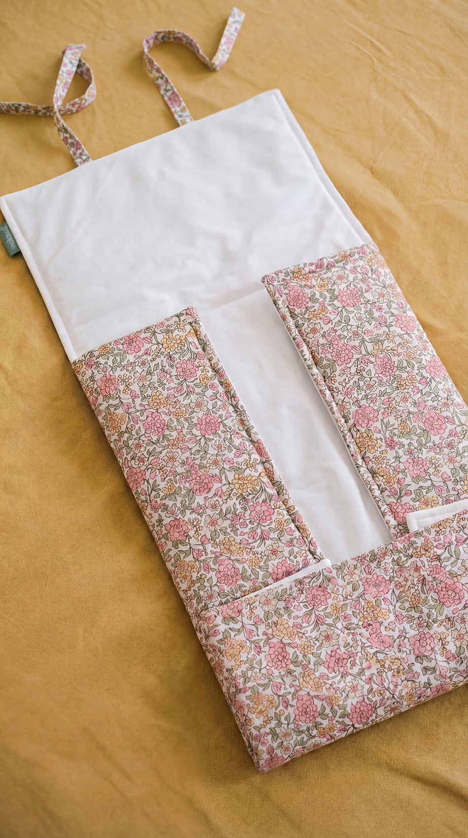 Organizador de tecido floral rosa e amarelo com alças sobre tecido castanho.