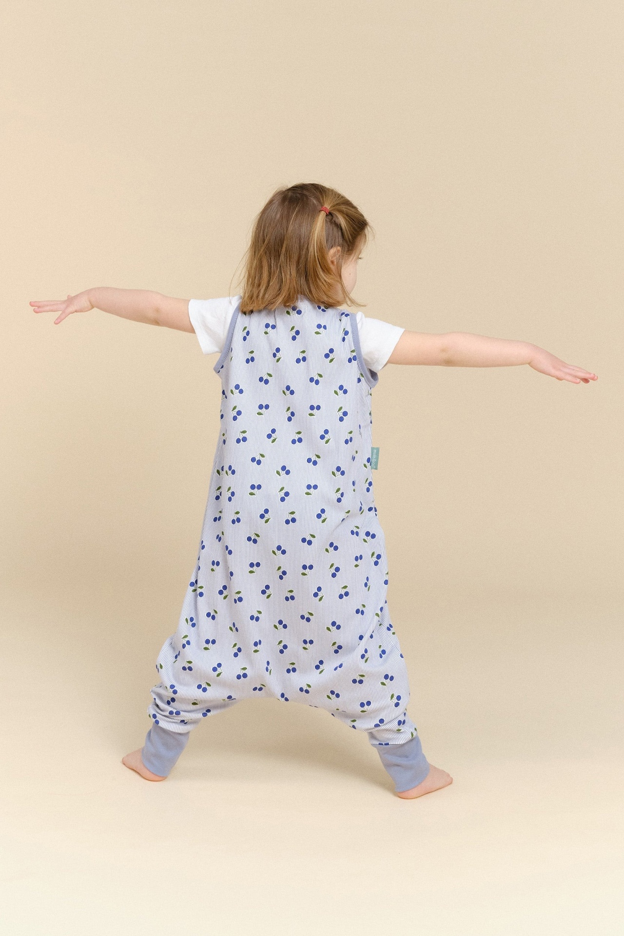 Criança de costas com camisola de dormir azul clara com padrão de cerejas e t-shirt branca