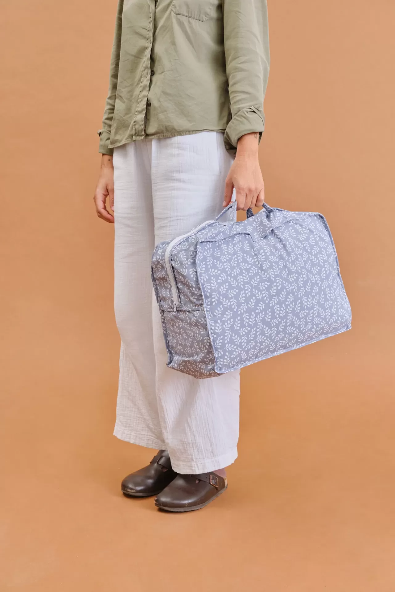 Mala azul claro com padrão de folhas em tecido, segurada por pessoa com roupa casual