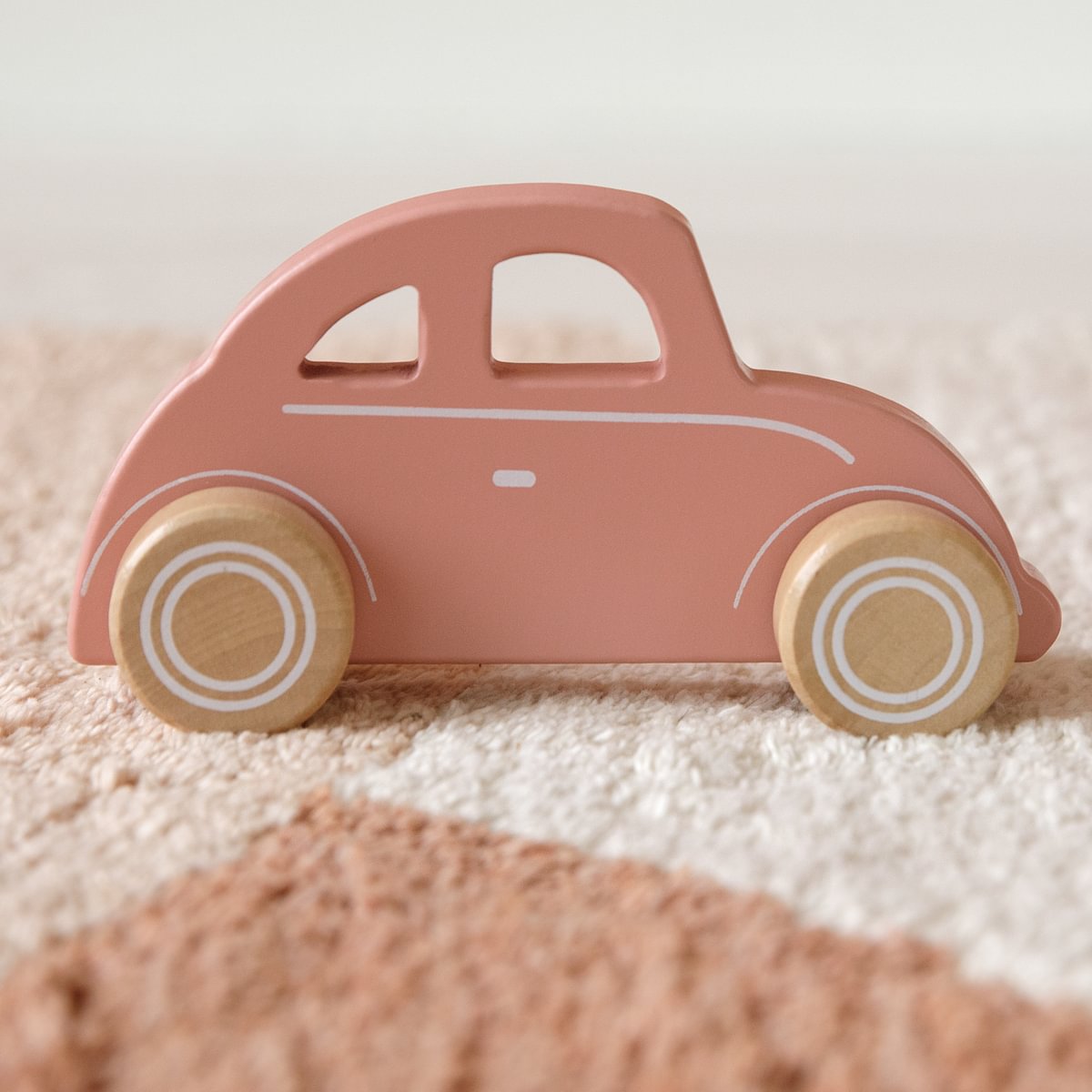 Brinquedo de carro de madeira rosa claro com rodas naturais em tapete