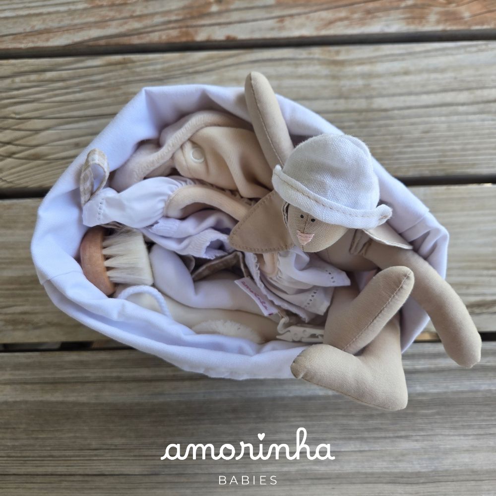 Cesto branco com boneco de tecido bege e pincel, sobre fundo de madeira