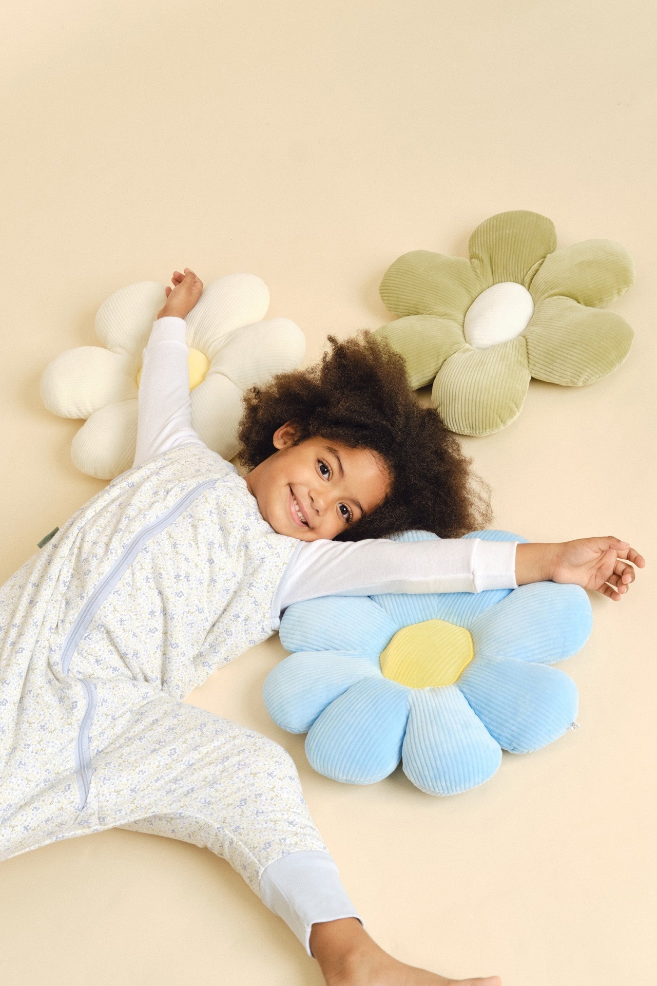 Criança sorridente deitada com roupa branca estampada com almofadas em forma de flor