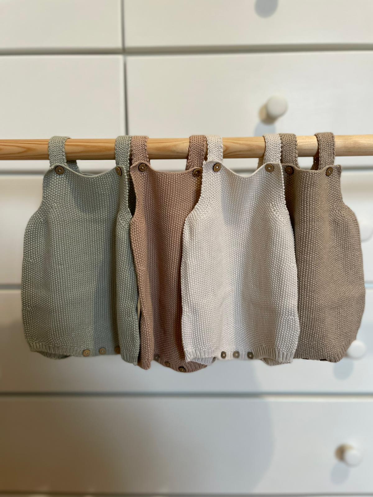 Vestidinhos de bebé em malha coloridos pendurados num cabide de madeira.