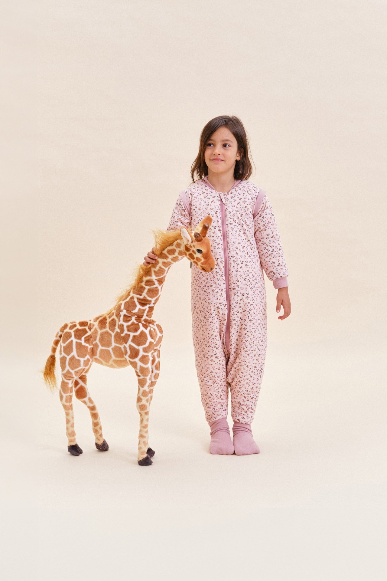 Criança com pijama rosa claro de padrão floral segurando peluche de girafa grande