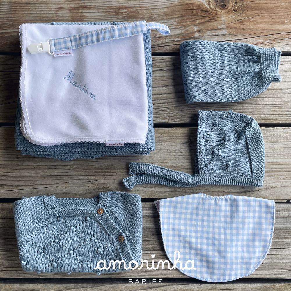 Conjunto de roupa de bebé tricot cinzento azulado com babetes e mantinhas, sobre madeira