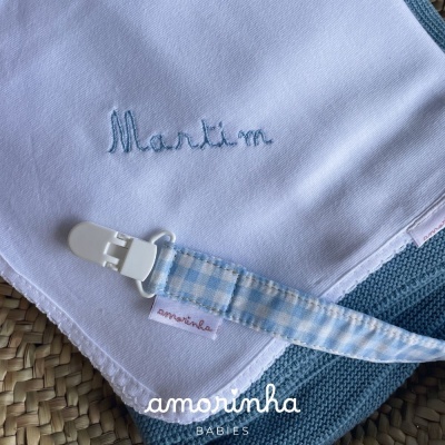 Babete branca bordada e suporte de chupeta azul com padrão xadrez