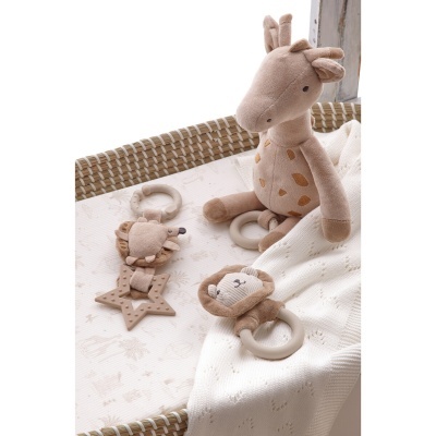 Brinquedos de bebé com girafa de peluche e anéis com leões numa cama de verga com manta branca