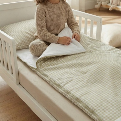 Criança em berço branco com saco de dormir bege xadrez e brinquedos ao fundo