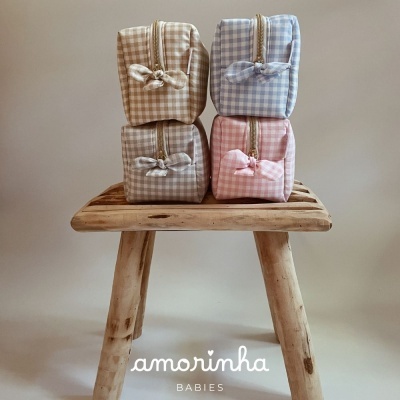 Quatro bolsas de tecido xadrez nas cores bege, azul, cinza e rosa sobre banco de madeira