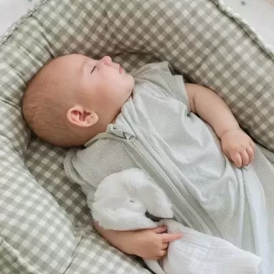 Bebé dormindo com saco de dormir cinzento em almofada xadrez verde e branco