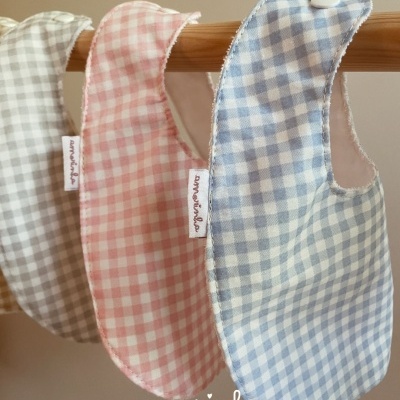 Três babetes xadrez para bebés em azul, rosa e cinza pendurados numa vara de madeira