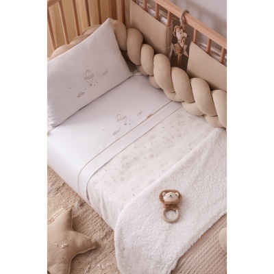 Berço de bebé com roupa de cama branca e bege, protetor trançado, peluche de leão e almofada estrela.