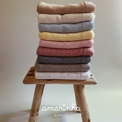 Camisolas de malha coloridas empilhadas sobre banco de madeira com texto amorinha BABIES