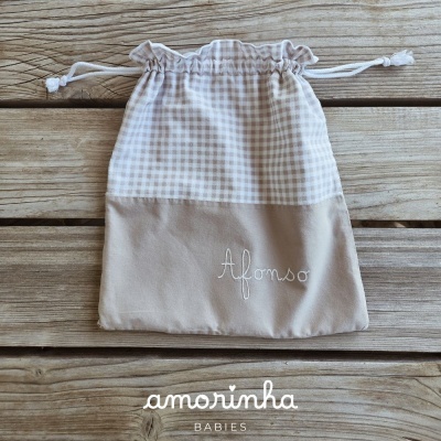 Saco de tecido bege com padrão xadrez e nome bordado Afonso, cordão de fecho sobre madeira