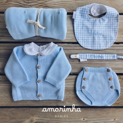 Conjunto de roupa e acessórios de bebé em tons de azul claro sobre madeira
