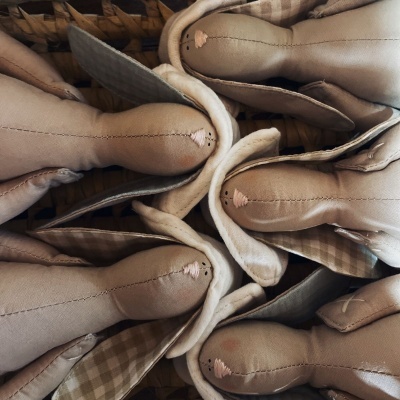 Coelhos de peluche em tecido bege com orelhas xadrez numa cesta de verga