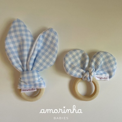 Dois mordedores de bebé azuis com argolas de madeira e padrão de quadrícula branca.