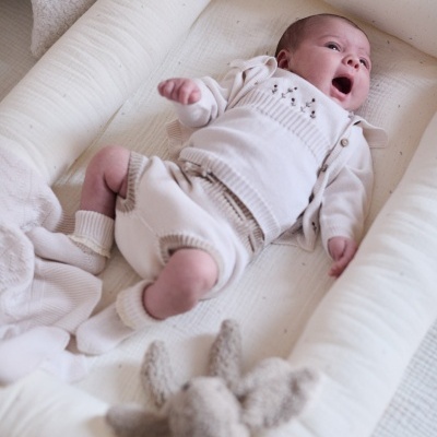 Berço acolchoado branco com bebé vestido de malha creme e brinquedo de peluche cinzento