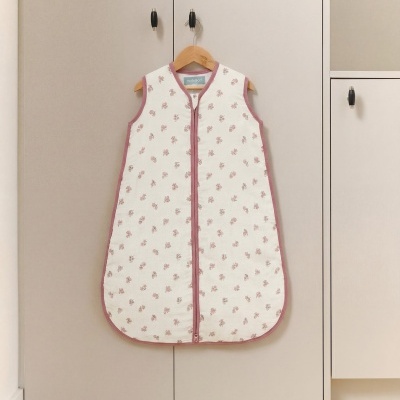 Saco de dormir para bebé branco com flores cor-de-rosa pendurado num armário cinzento