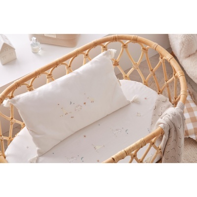 Berço de vime com colchão branco e almofada decorativa com desenhos de animais e estrelas.