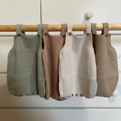 Vestidinhos de bebé em malha coloridos pendurados num cabide de madeira.