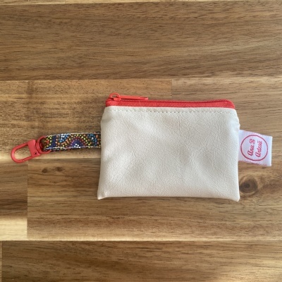 Bolsa pequena branca com fecho vermelho e alça colorida sobre superfície de madeira