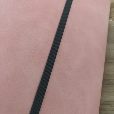 Caderno rosa com elástico preto numa mesa de madeira.