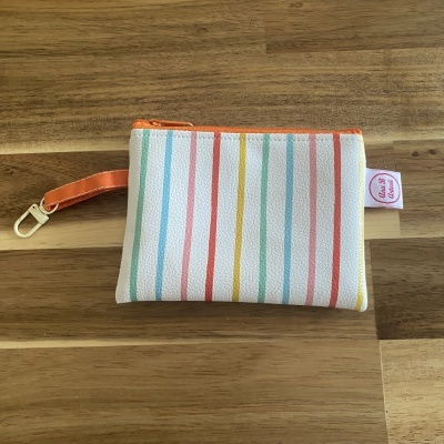 Necessaire pequena branca de riscas coloridas com fecho e alça laranja sobre mesa de madeira