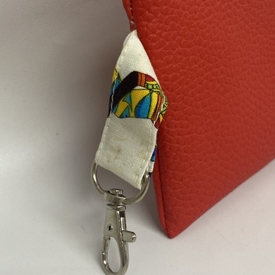 Pequena mala vermelha com fecho azul e alça estampada com mosquetão