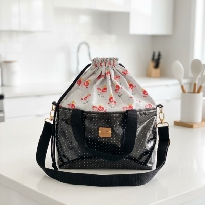 Bolsa preta com pontos brancos e parte superior em tecido branco com flores vermelhas sobre bancada branca
