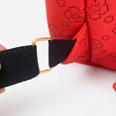 Detalhe de bolsa vermelha com estampa floral preta e alça preta com fivela dourada