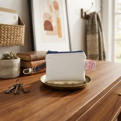 Necessaire branca com fecho azul e alça colorida numa base metálica sobre mesa de madeira