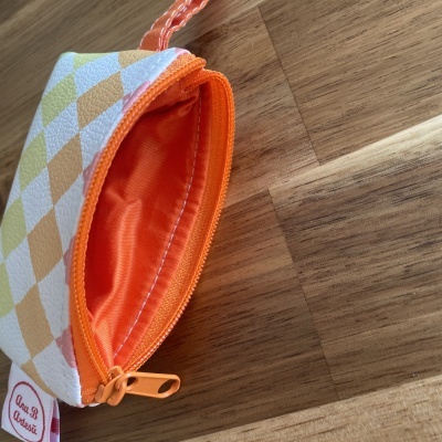 Bolsa pequena com padrão de losangos pastel e interior laranja sobre superfície de madeira