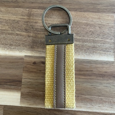 Chaveiro com argola metálica e tira amarela com faixa castanha sobre madeira