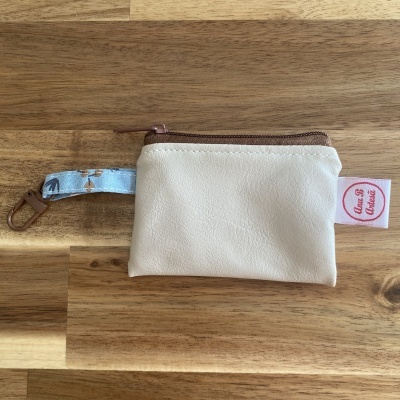 Bolsa pequena creme com fecho castanho e alça azul estampada sobre mesa de madeira.