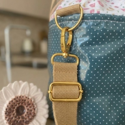 Bolsa azul às bolinhas com alça bege e metais dourados e objeto decorativo de flor