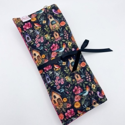 Estojo de tecido estampado com casinhas de pássaros e flores, fechado com fita preta.