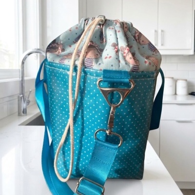 Mochila azul turquesa com padrão de bolinhas brancas e desenho infantil com personagens, alça ajustável e cordão de fecho.