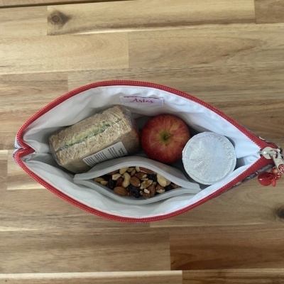 Bolsa térmica aberta com sanduíche, maçã, recipiente e frutos secos em fundo de madeira