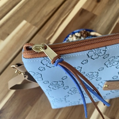 Mala azul clara com padrão floral e fecho de correr castanho.