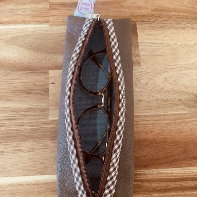 Estojo para óculos castanho com padrão xadrez e óculos dentro sobre mesa de madeira.