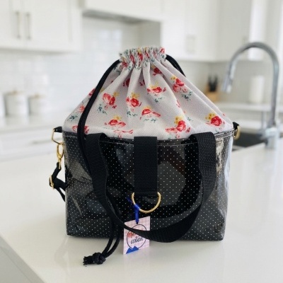 Mala de mão preta com base transparente de pontos brancos e interior floral, alças pretas, em bancada de cozinha