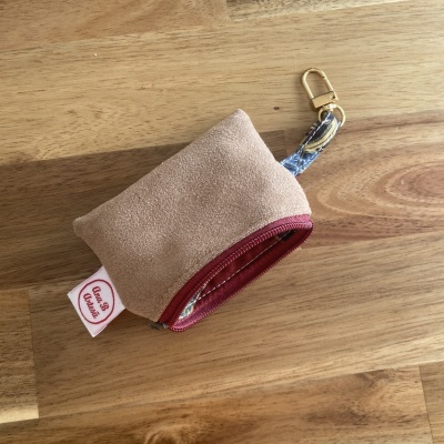 Bolsa pequena castanha com fecho vermelho e alça estampada com mosquetão dourado sobre madeira