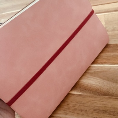 Caderno cor-de-rosa com elástico vermelho sobre mesa de madeira