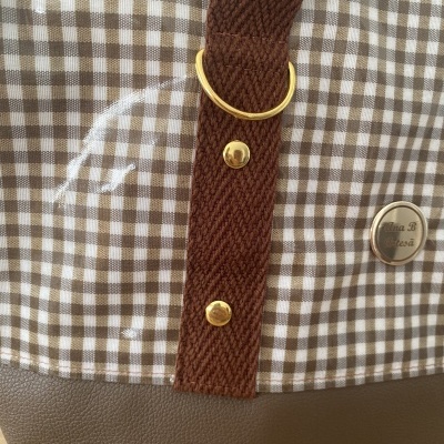 Parte de bolsa com padrão xadrez castanho e branco, alça castanha e detalhes dourados.