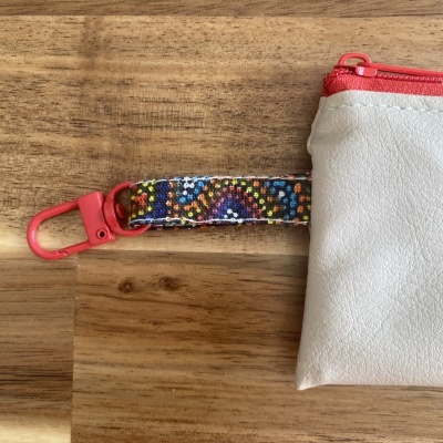 bolsa pequena branca com fecho vermelho e fita colorida sobre madeira