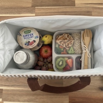 Lancheira aberta com iogurtes, fruta, recipiente com comida e utensílios embalados.