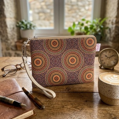 Bolsa de mão com padrão mandala em tons terra sobre mesa de madeira junto a caderno, canetas e chávena de café