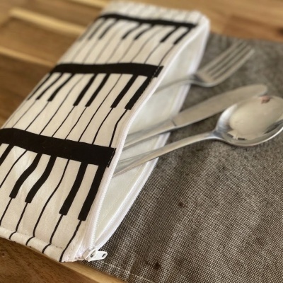 Estojo branco com padrão de teclas de piano com talheres de metal sobre tecido cinza e mesa de madeira